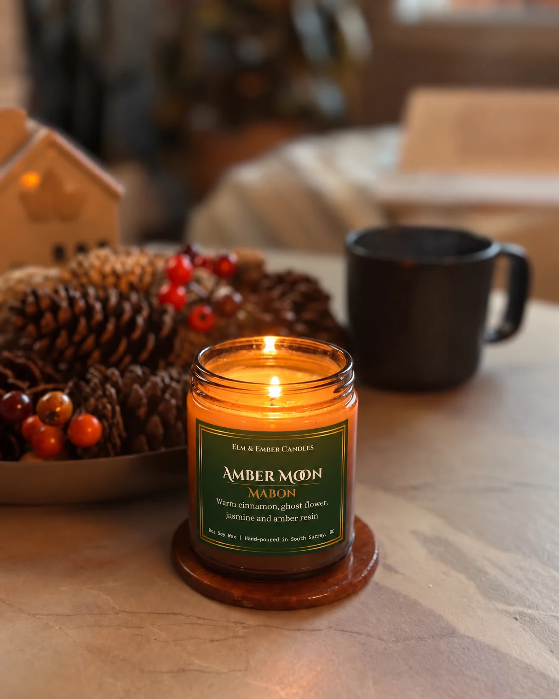 Amber Moon candle lit beside pinecones and red berries