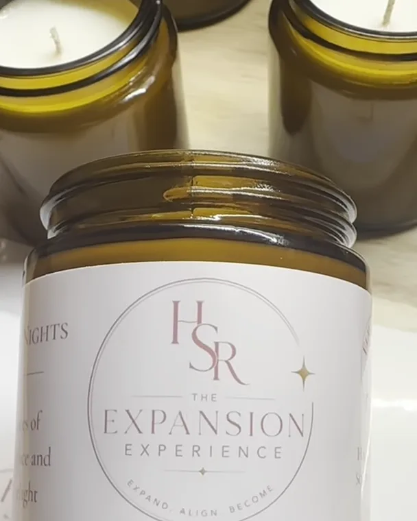 A hand holding a candle with a custom blush label, in front of rows of freshly poured jars