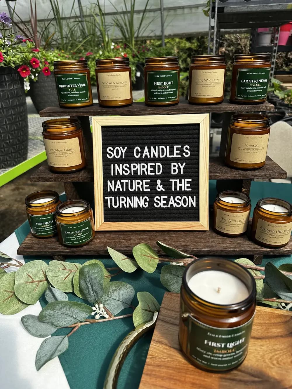 Our market table: Wheel and Wildwood candles on wooden risers around a letter board that reads Soy candles inspired by nature and the turning season