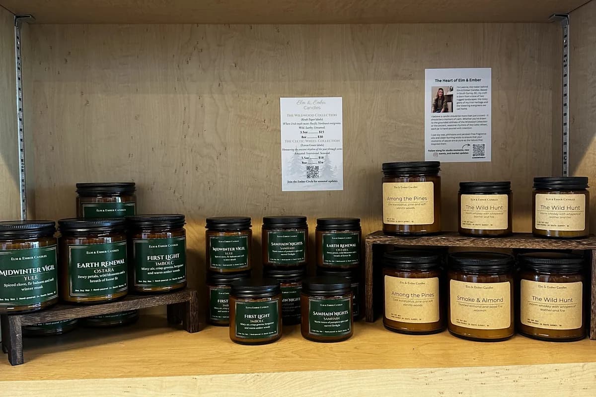 Elm & Ember candles on a wooden shelf between bottles of Otter Trail wine